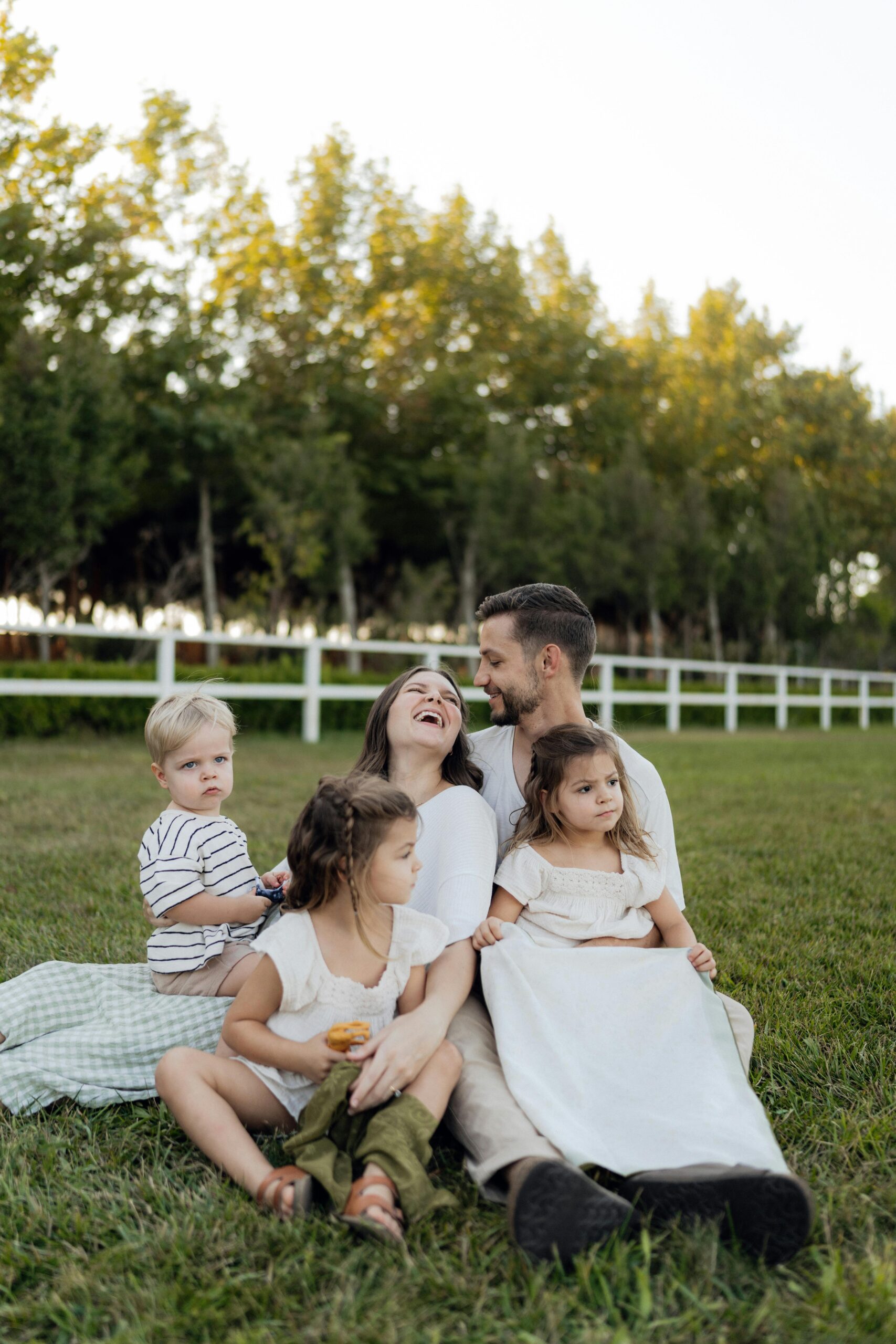 Family of five laughing and enjoying a sunny day on the grass with a forest background.